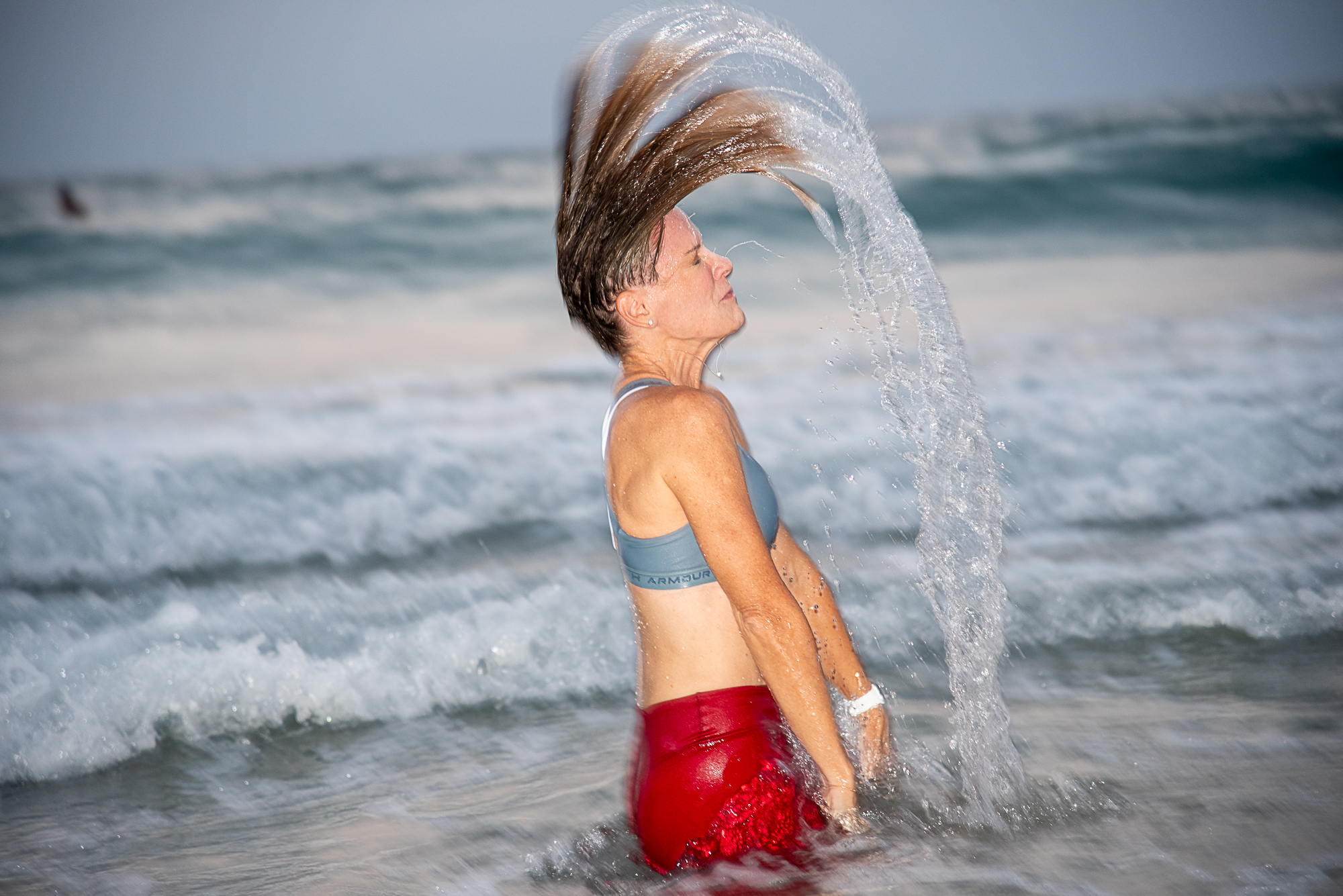 אורית אנגלשטיין בים מניפה את שערה לאחור כך שנוצרת קשת של מים מעלייה.